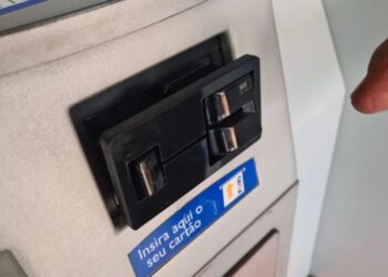 Uma tentativa de golpe bancário foi frustrada após o sistema antifraude de uma instituição financeira bloquear movimentações suspeitas e evitar um prejuízo superior a R$ 13 mil a um cliente. O caso ocorreu dentro de uma agência bancária em Formiga, no Centro-Oeste de Minas Gerais, e resultou na prisão de três homens. De acordo com a Polícia Militar, os suspeitos adulteraram o leitor biométrico de caixas eletrônicos para dificultar o acesso dos clientes às contas. A situação chamou a atenção após movimentações atípicas serem identificadas pelo sistema de segurança do banco, o que levou à interrupção da fraude ainda no local. A vítima, um homem com interdição jurídica parcial, apresentou dificuldades para utilizar o caixa eletrônico. Nesse momento, um dos suspeitos se aproximou, se passando por funcionário da agência, e ofereceu ajuda. Com o apoio de comparsas, o grupo cadastrou chaves de segurança e senhas da conta da vítima em aparelhos celulares pertencentes aos próprios criminosos. Com os dados obtidos, os suspeitos chegaram a realizar três empréstimos bancários, que totalizaram R$ 13.217,88. A transferência dos valores, no entanto, não foi concluída devido ao bloqueio preventivo realizado pelo sistema antifraude da instituição. Após analisarem imagens do circuito interno de monitoramento, os policiais identificaram o veículo utilizado no crime e a possível rota de fuga. As equipes se posicionaram na saída da cidade em direção à BR-354, onde abordaram o carro, que tinha placas do Rio de Janeiro e vidros escuros. Inicialmente, os três homens, com idades de 27, 44 e 45 anos, negaram o crime e alegaram que apenas consultavam saldos bancários. Contudo, as imagens e demais provas reunidas confirmaram a participação deles no esquema. Segundo a PM, o grupo já era suspeito de aplicar golpes semelhantes em outras cidades de Minas Gerais, como Patrocínio. Durante a ação, foram apreendidos três aparelhos celulares e R$ 554 em dinheiro. O veículo utilizado foi removido para um pátio credenciado, e os suspeitos foram presos em flagrante e encaminhados à delegacia.